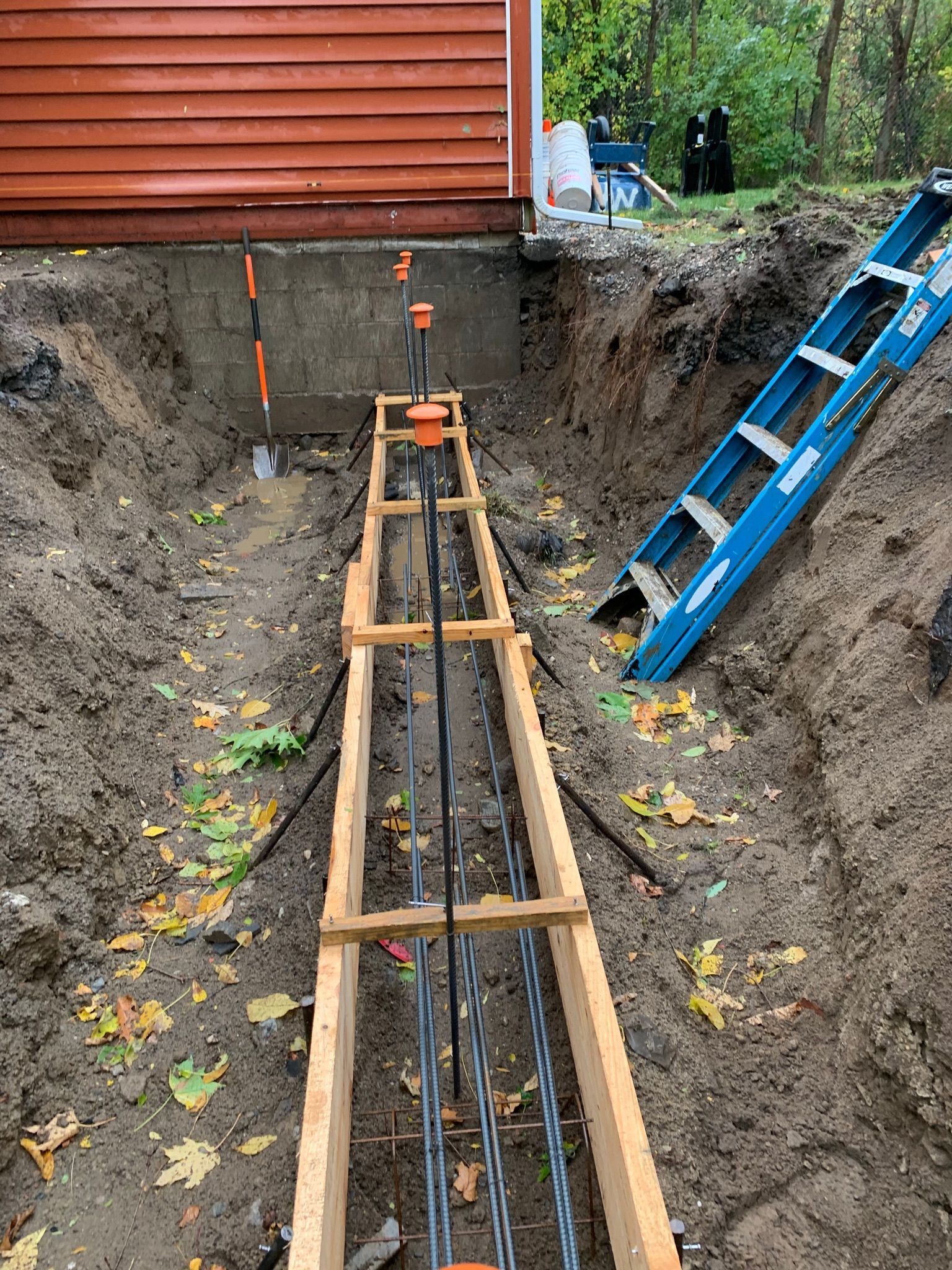 A ladder is sitting in the dirt next to a wooden beam.