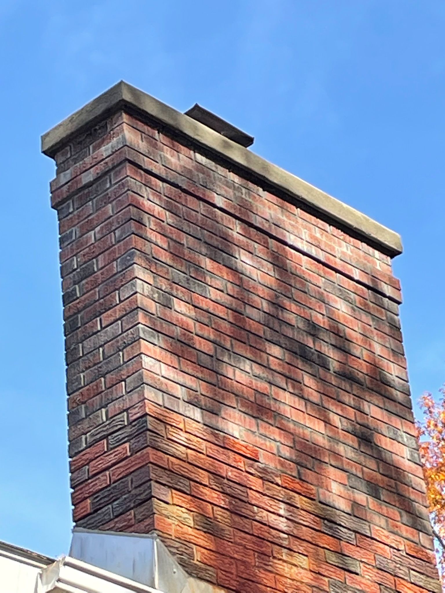 A large brick chimney on top of a house with a blue sky in the background.