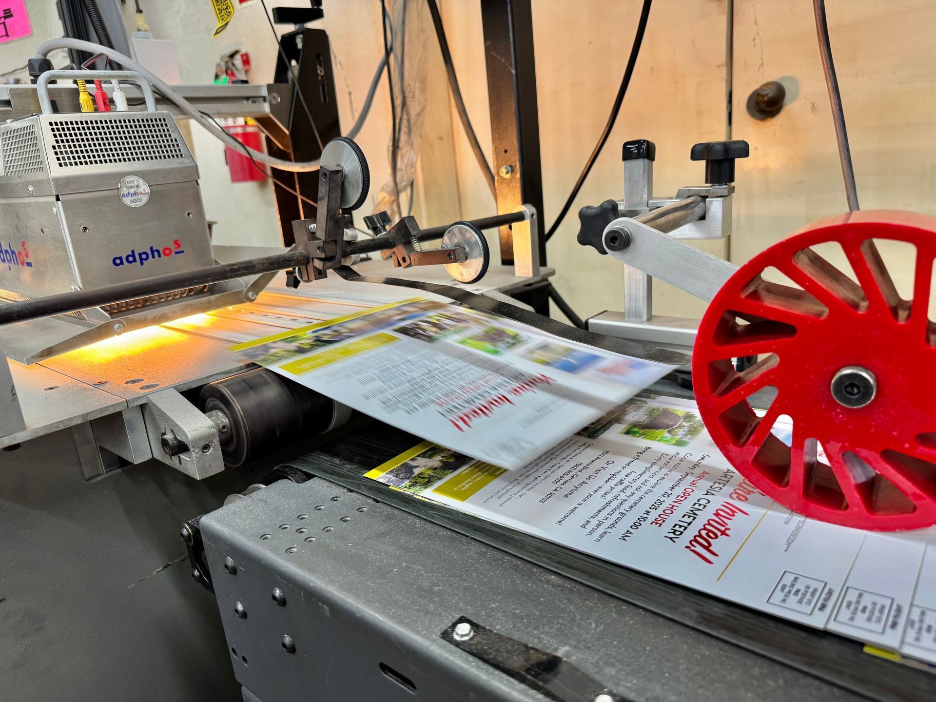 Brochures being folded by a printing machine, red wheel visible.
