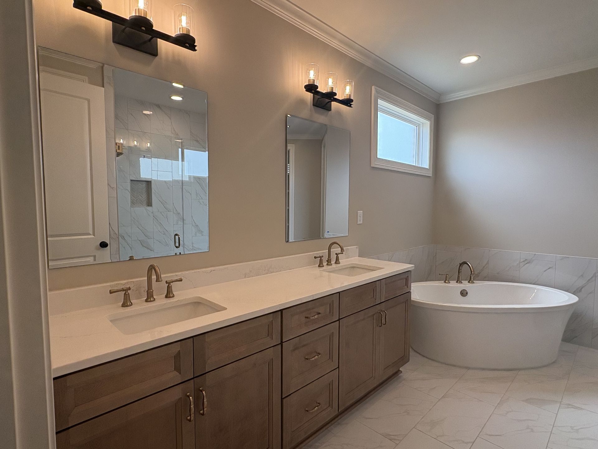 Bright bathroom with double vanity, mirrors, wall sconces, and a freestanding soaking tub.