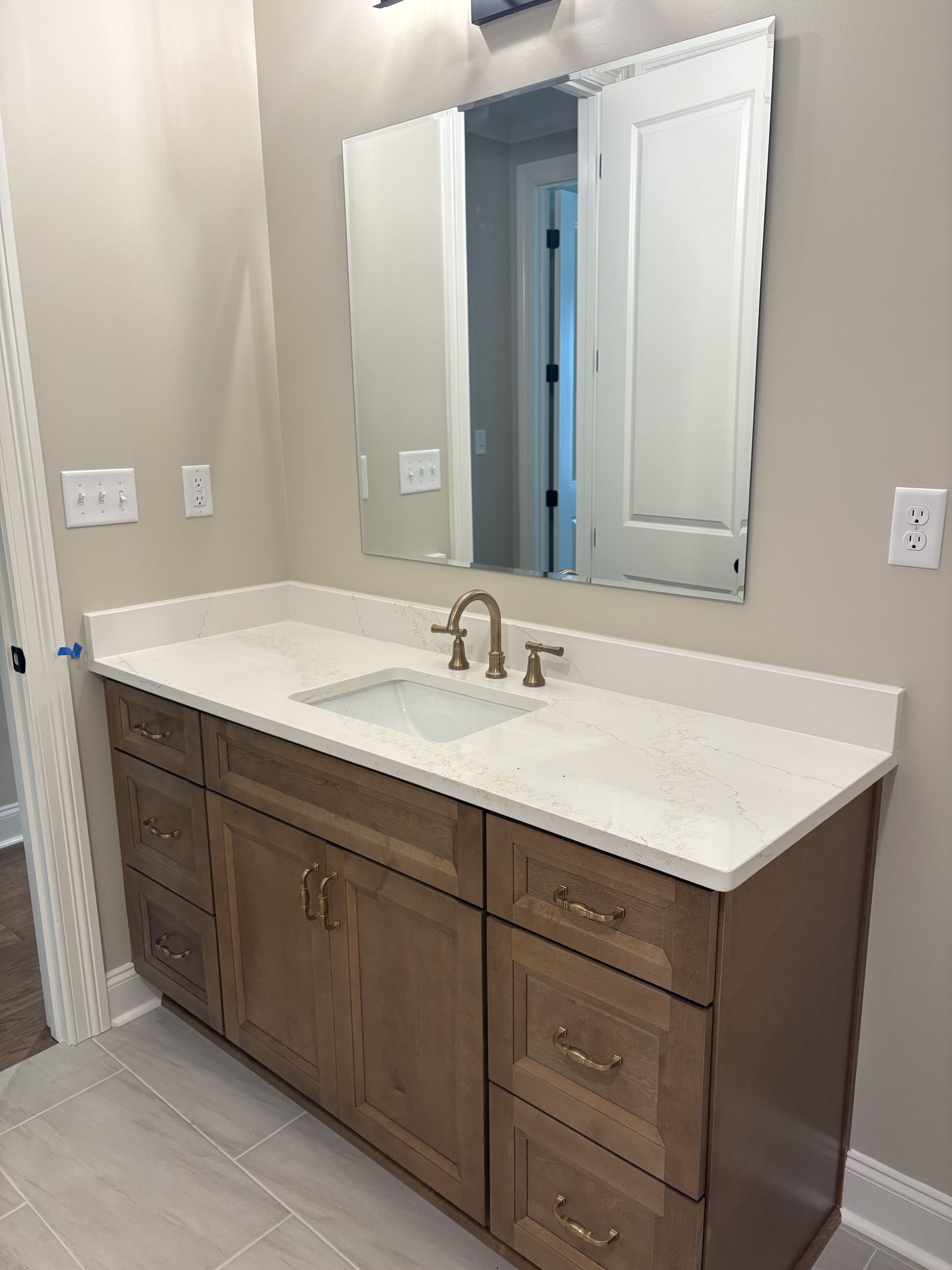 Bathroom vanity with white countertop, double mirrors, and wood cabinets against beige walls.