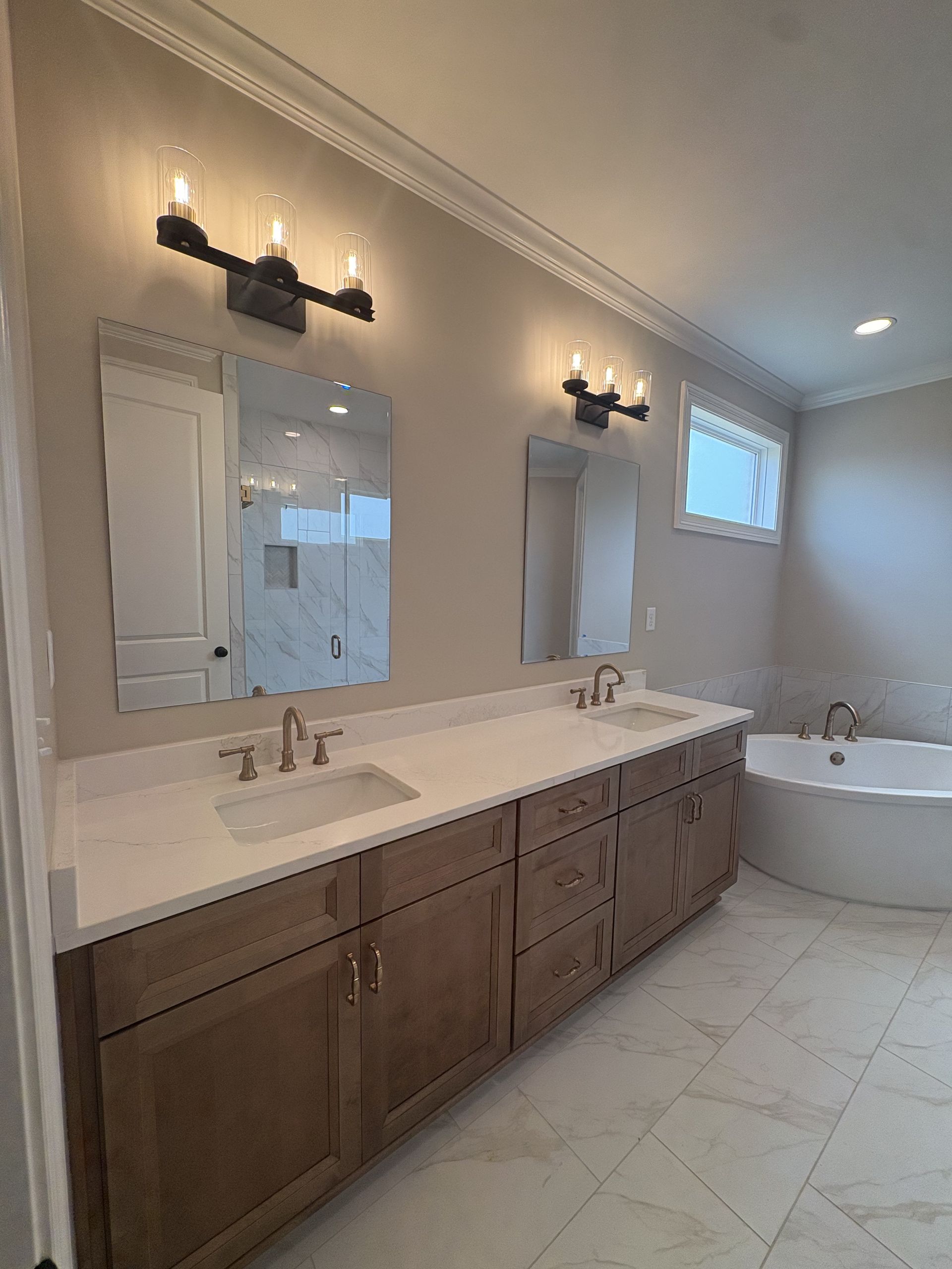 Elegant bathroom with double vanity, wall sconces, and a freestanding tub in a light, tiled space