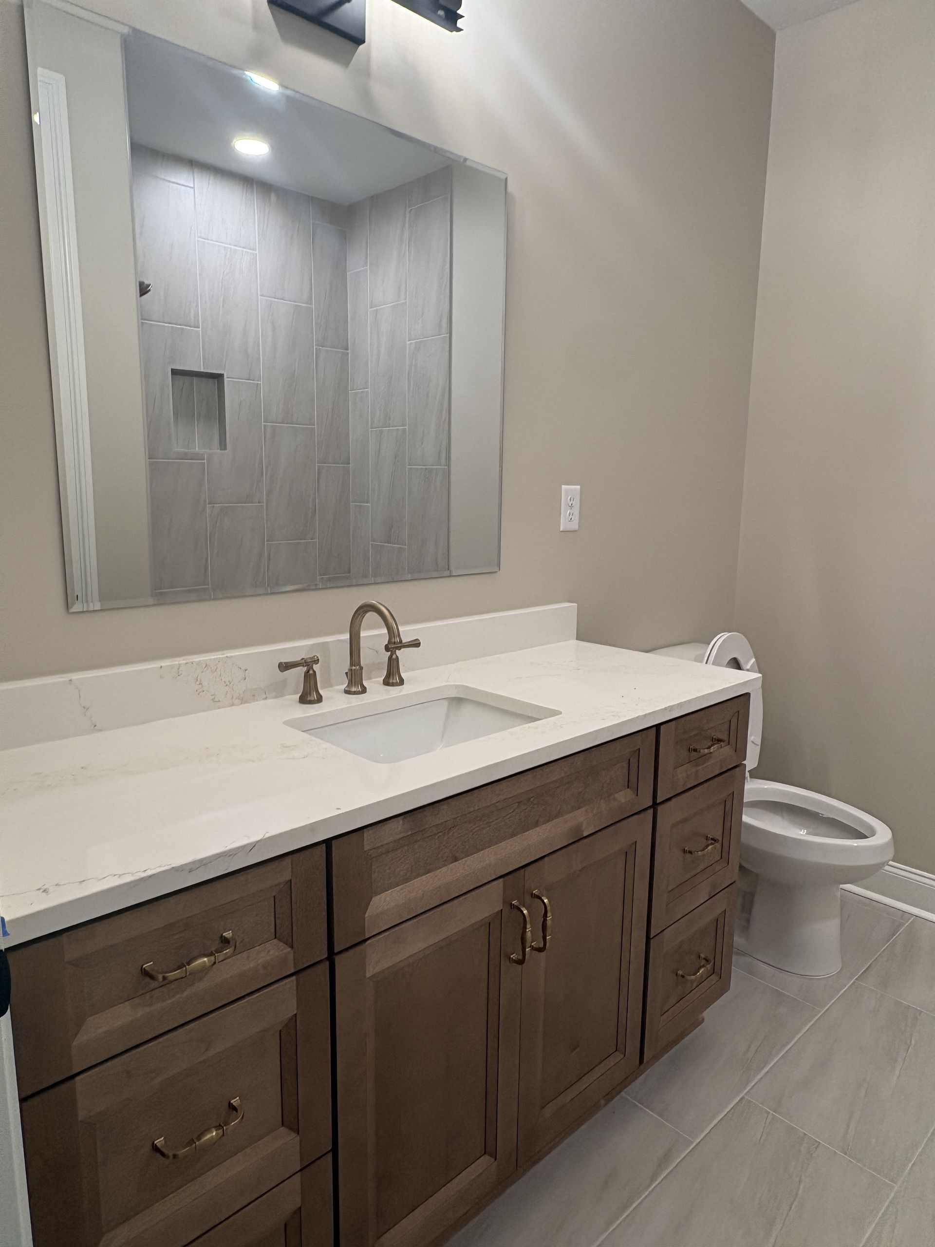 Bathroom with wood vanity, white countertop, mirror, and toilet on gray tile floor.