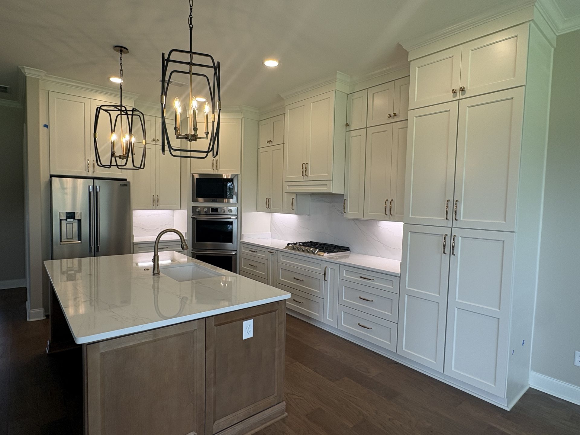 Bright white kitchen with island, pendant lights, stainless appliances, and wood floor.