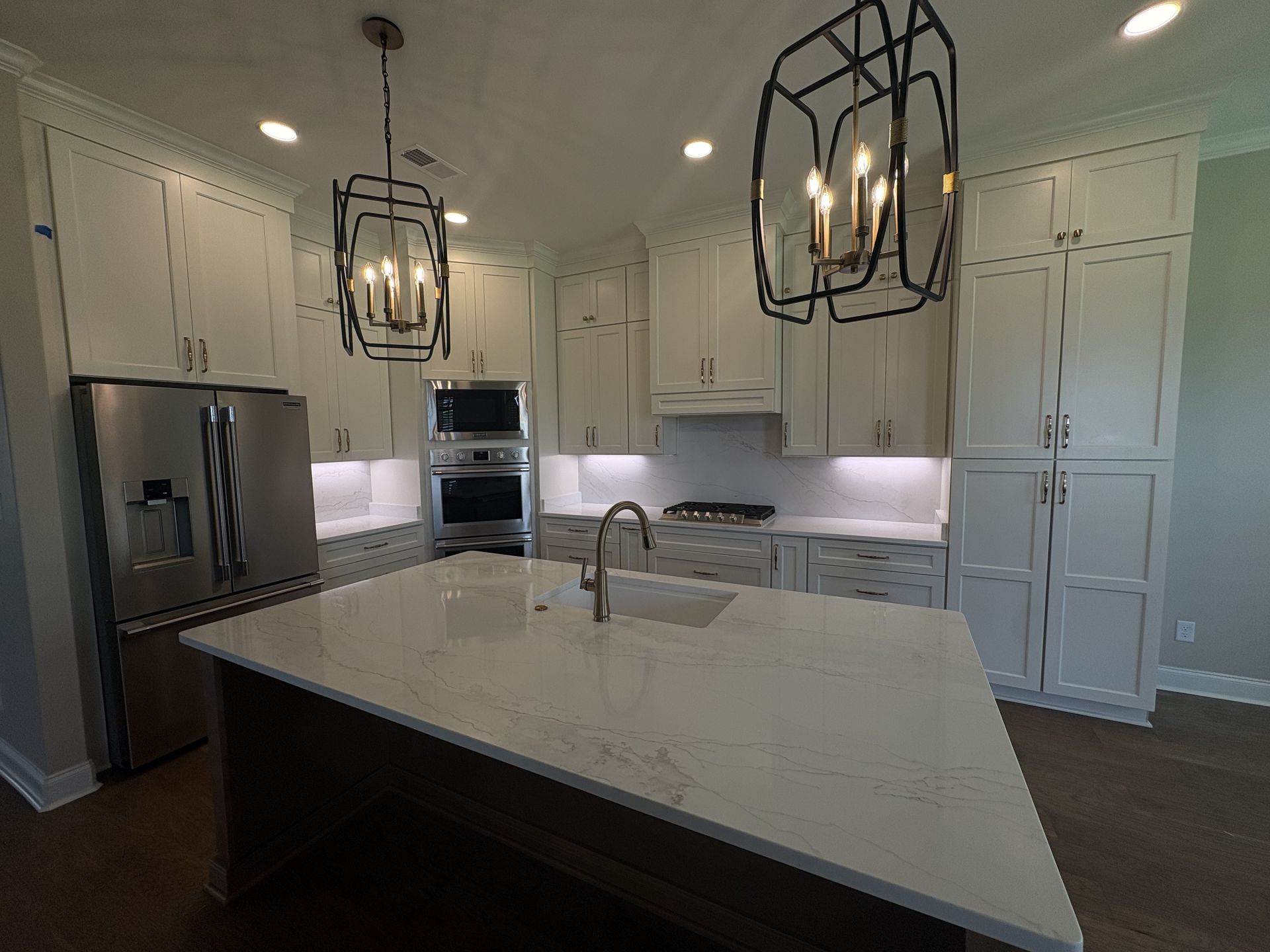 Modern white kitchen with large island, stainless appliances, and black pendant lights