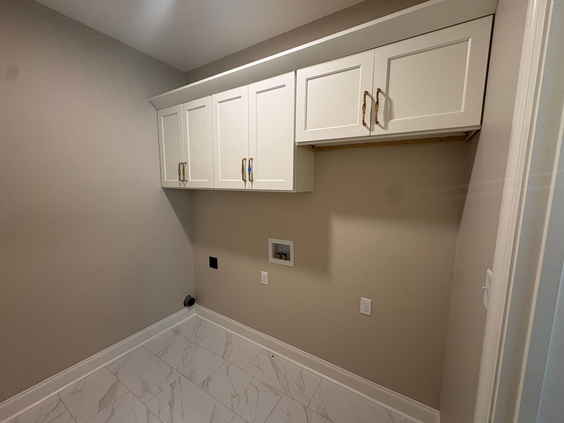 Empty laundry room with white cabinets, beige walls, and patterned tile flooring