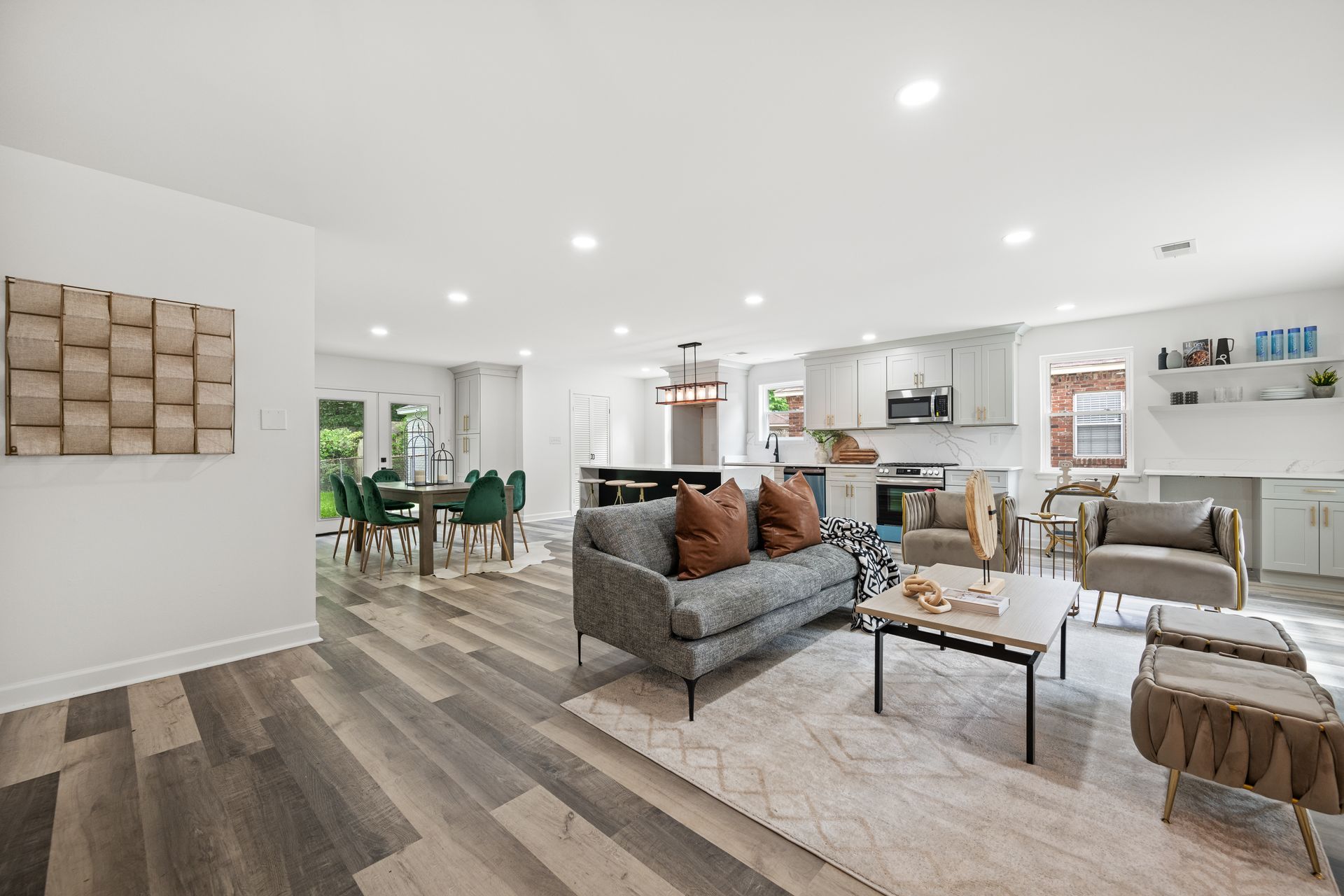 Open-concept living space with gray sofa, kitchen, and dining area. Light wood-look flooring.