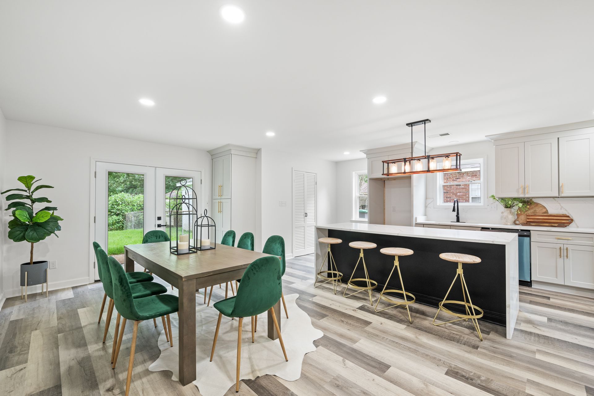 Open-plan kitchen and dining area with green velvet chairs, island with stools, and French doors to a yard.