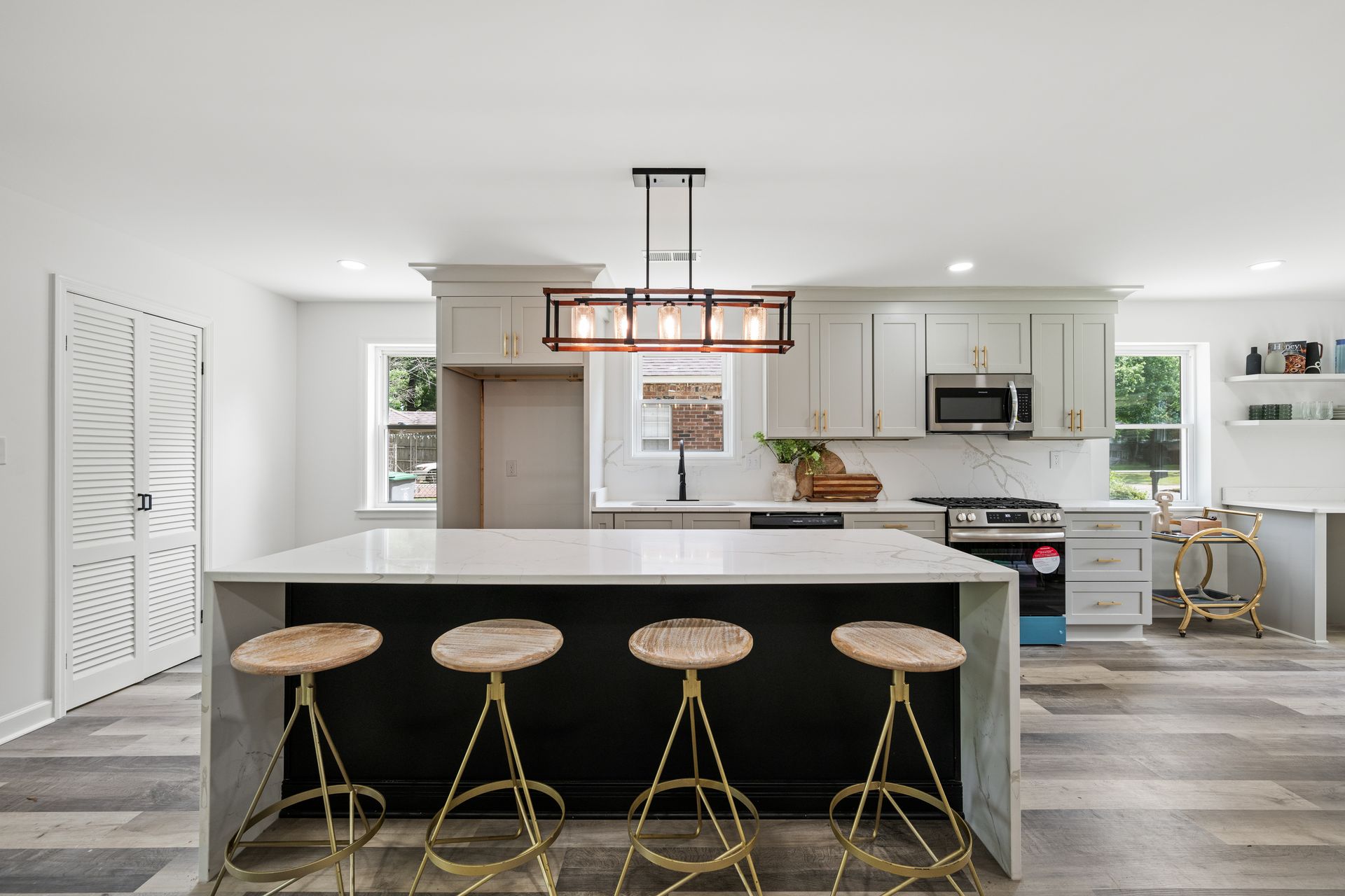 Modern kitchen with white cabinets, island with stools, and wooden floors.
