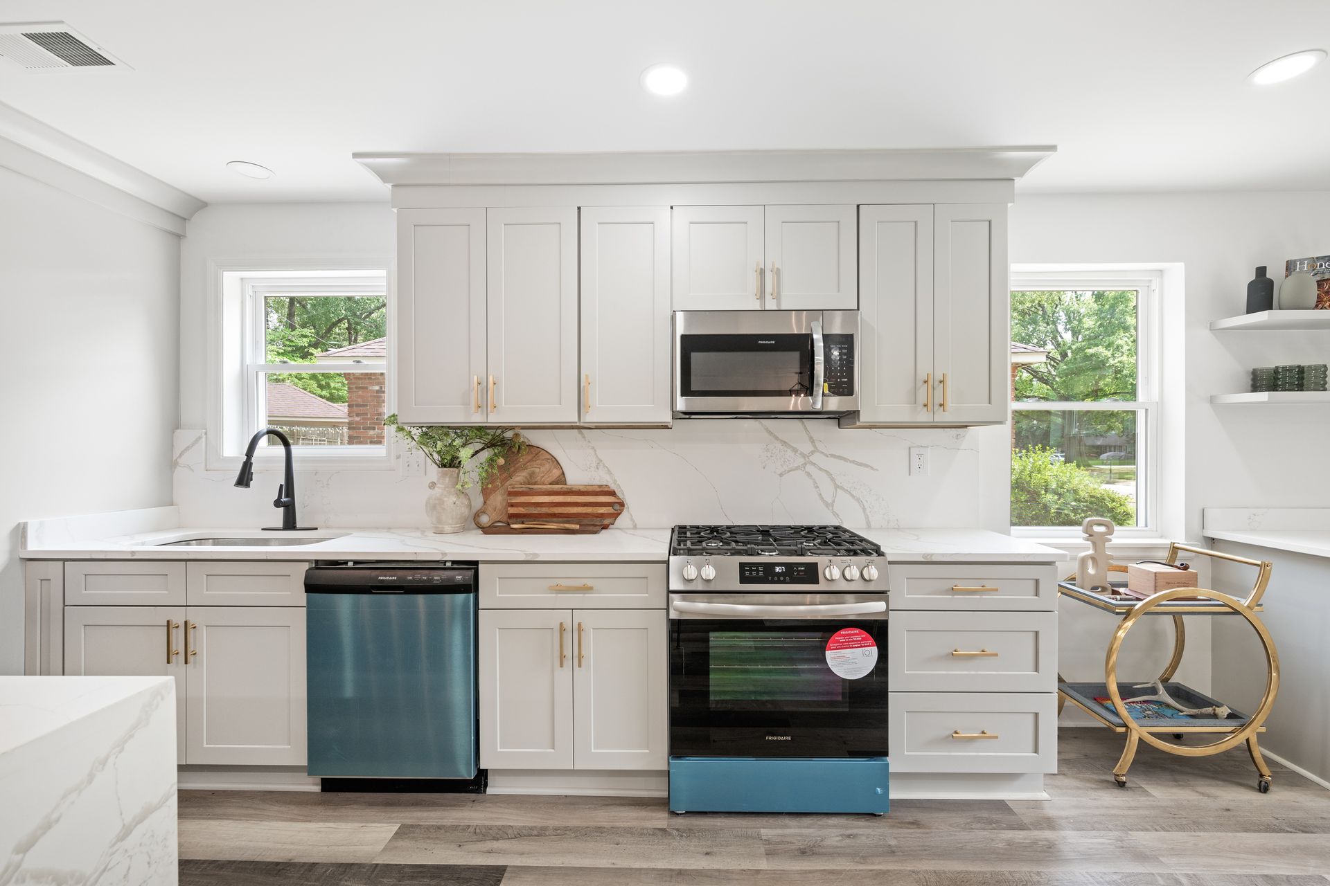 Modern white kitchen with stainless steel appliances, marble backsplash, and teal accents.