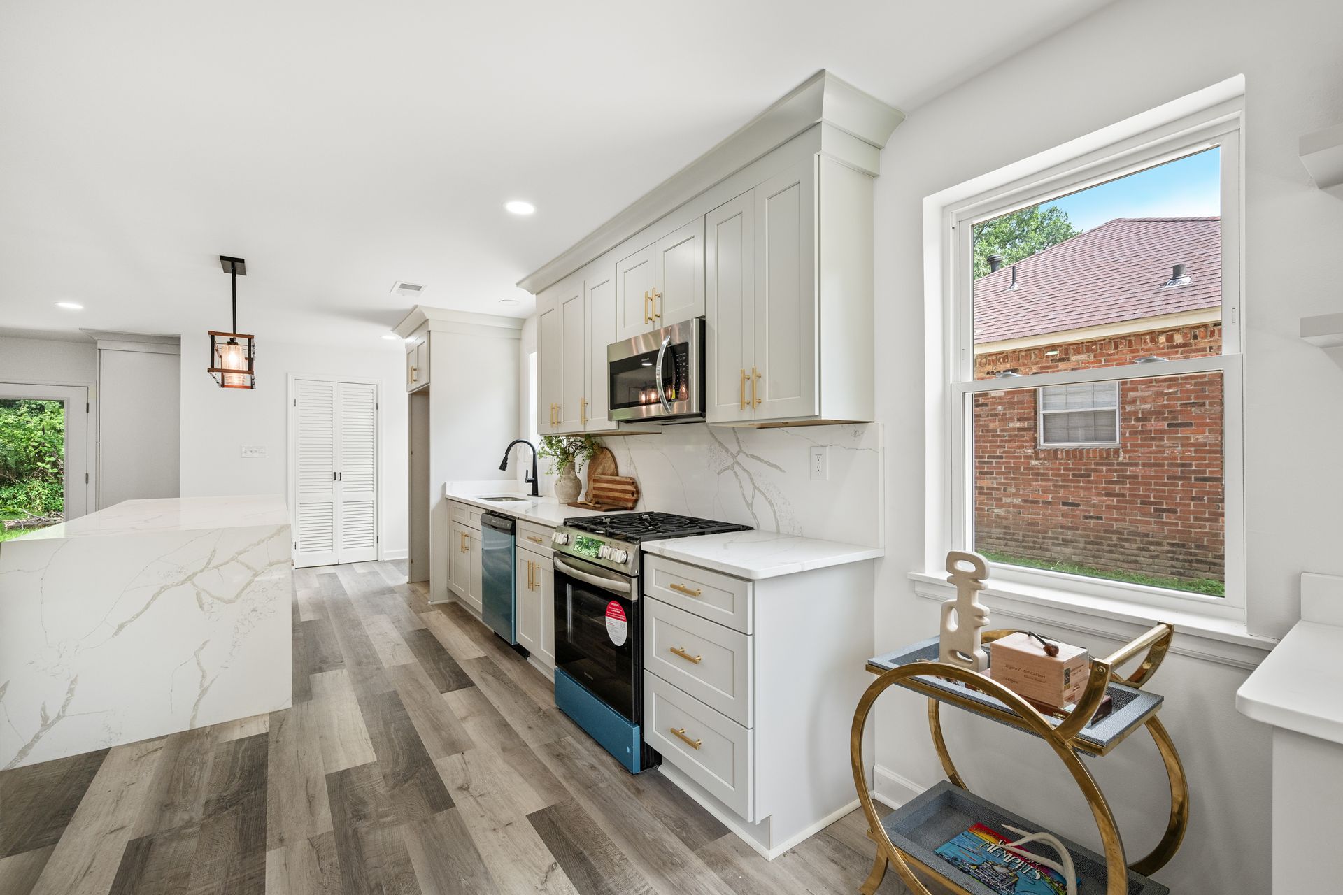 Modern kitchen with white cabinets, marble countertops, stainless steel appliances, and a window overlooking a brick building.