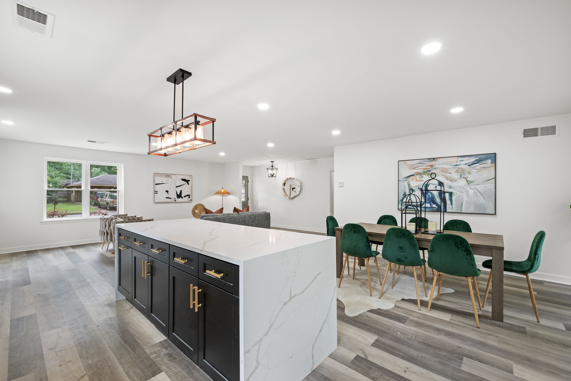 Modern open-concept kitchen and dining area with black island, green chairs, and wood flooring.