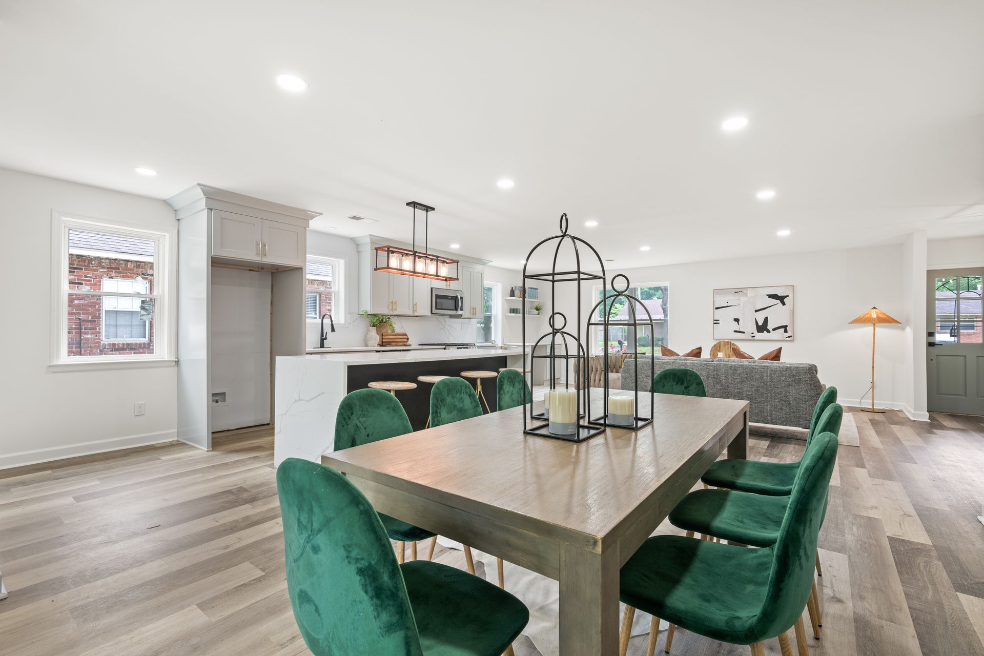 Open-concept dining and kitchen with a long wooden table and green chairs. Black and white decor.