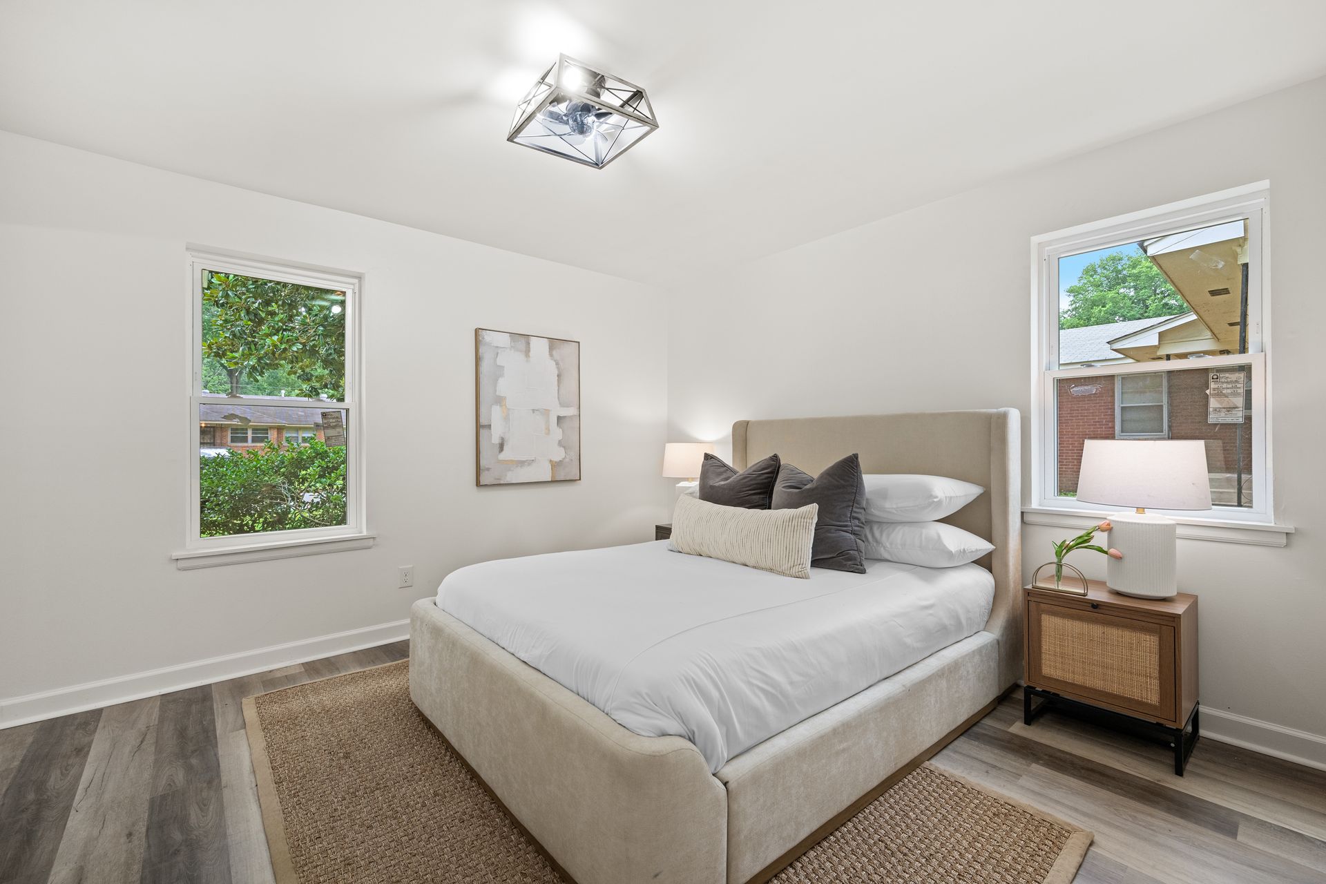 Bedroom with a bed, nightstand, windows, and neutral colors; natural light.