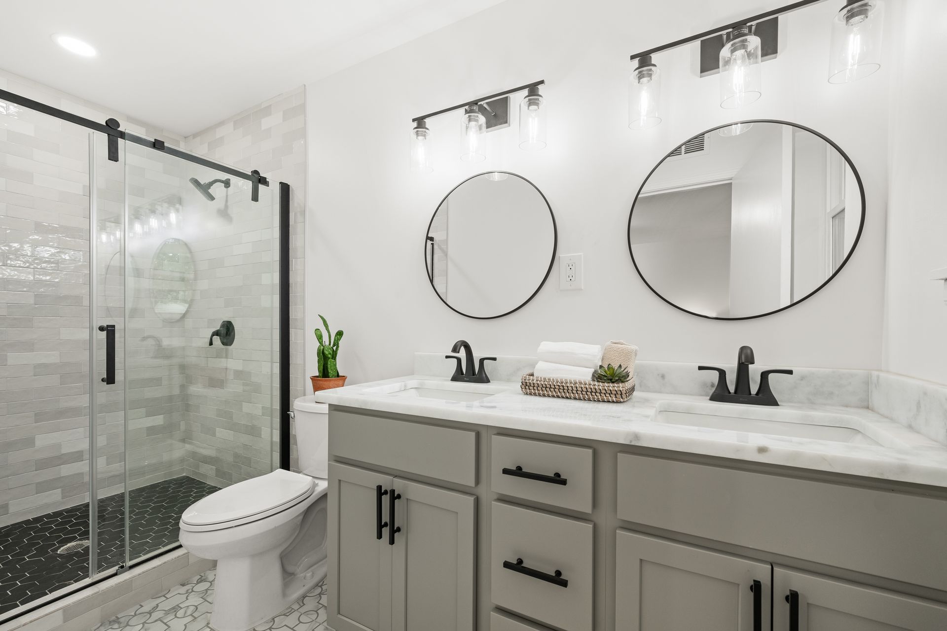 Modern bathroom with gray vanity, round mirrors, and glass shower.