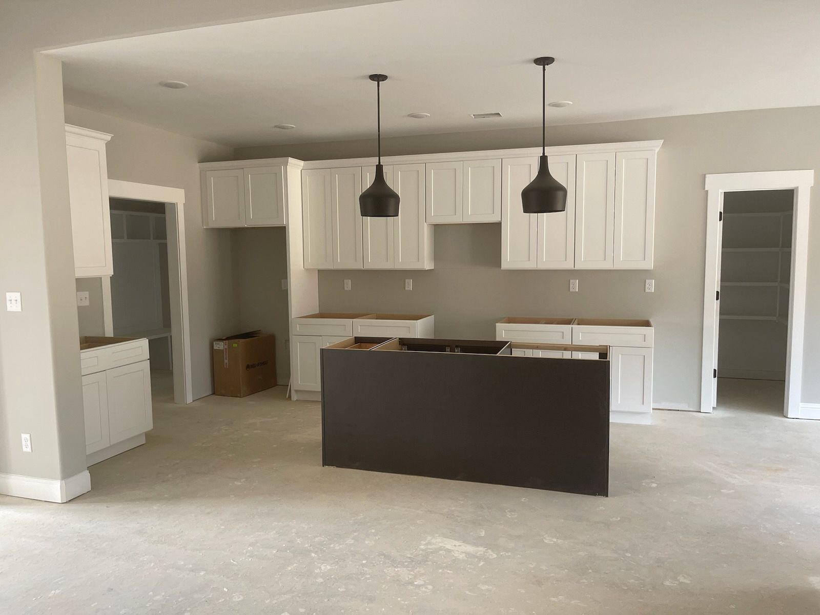 Kitchen with white cabinets, dark island, and two pendant lights. Construction site.