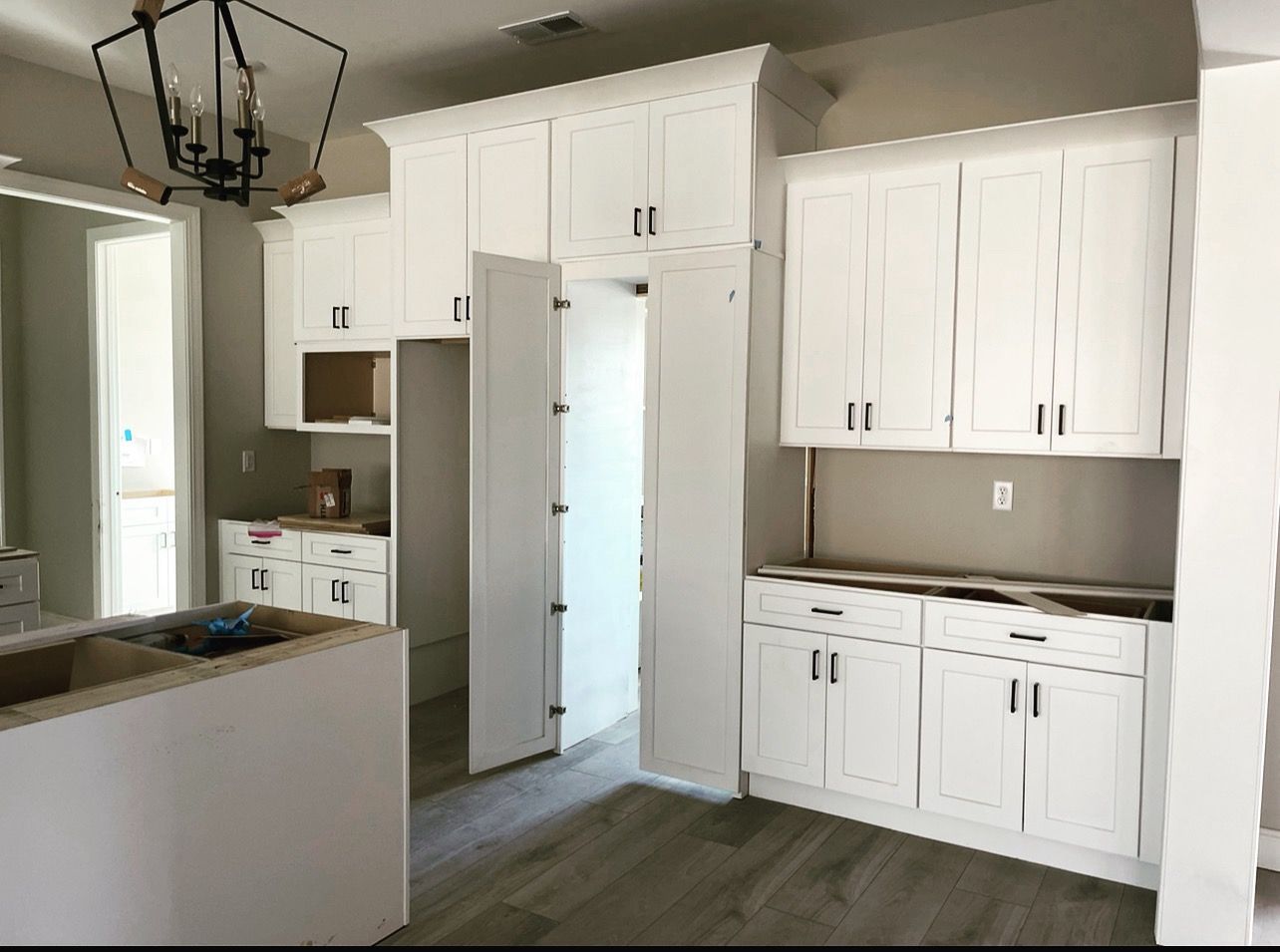 White kitchen cabinets installed in a room with light wood-look flooring and a chandelier.