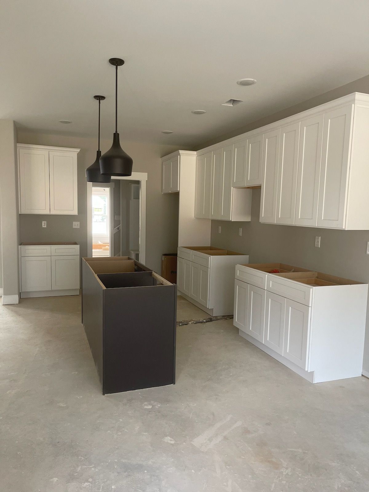 Kitchen with white cabinets, dark island, and pendant lights; under construction.