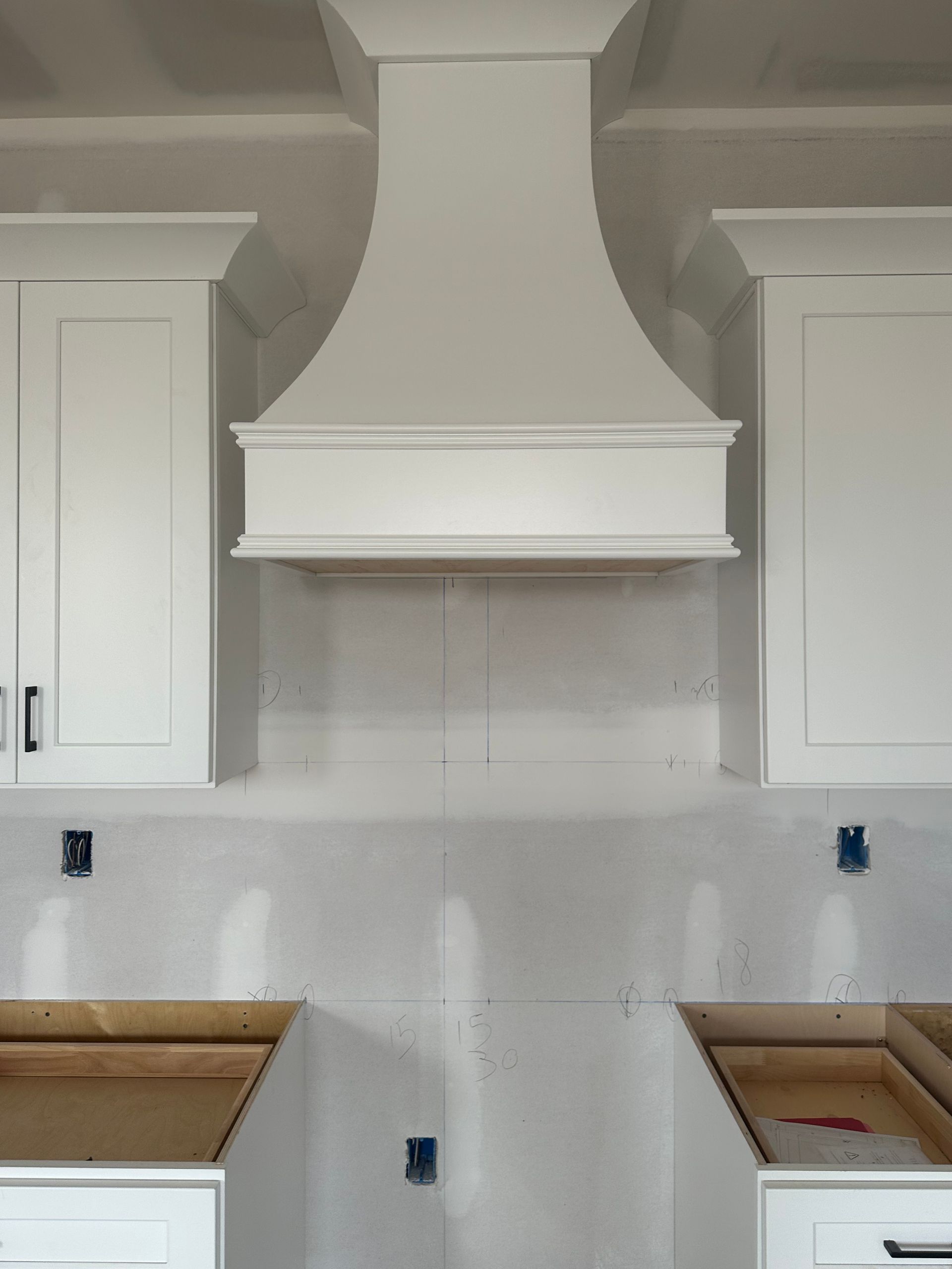 White kitchen range hood centered between white cabinets; unfinished drywall and cabinetry below.