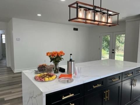 Modern kitchen with island, black cabinets, white countertop, flowers, and chandelier.