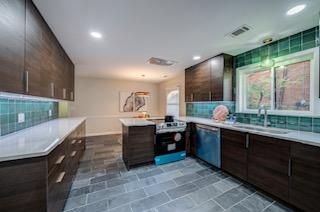 Modern kitchen with dark wood cabinets, white countertops, teal tile backsplash, and gray tile flooring.