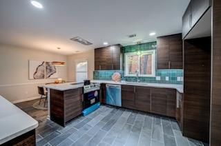 Modern kitchen with dark wood cabinets, gray tiled floor, and teal backsplash.