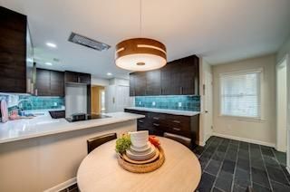 Modern kitchen with dark cabinetry, white countertops, teal backsplash, round table, and pendant light.