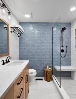 Bathroom with blue tiled shower, glass door, white bench, wooden vanity, and modern fixtures.