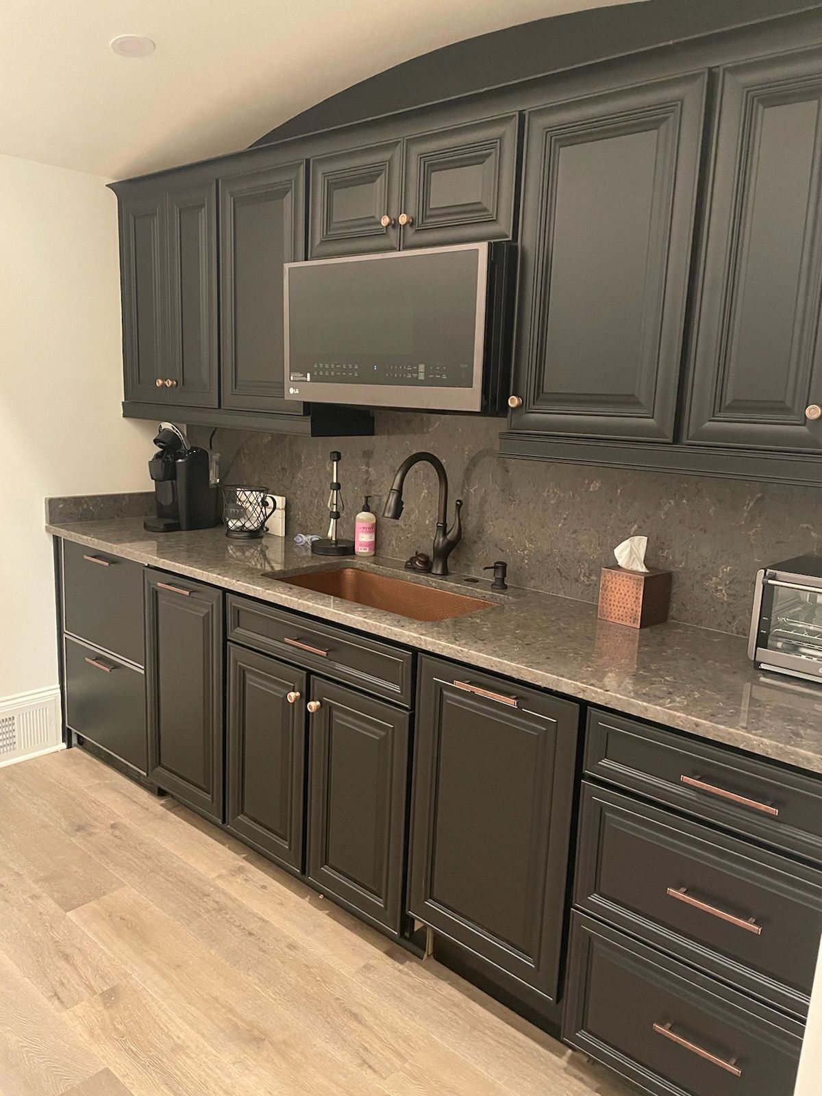 Black kitchen cabinets with a brown countertop, copper sink, and mounted TV.