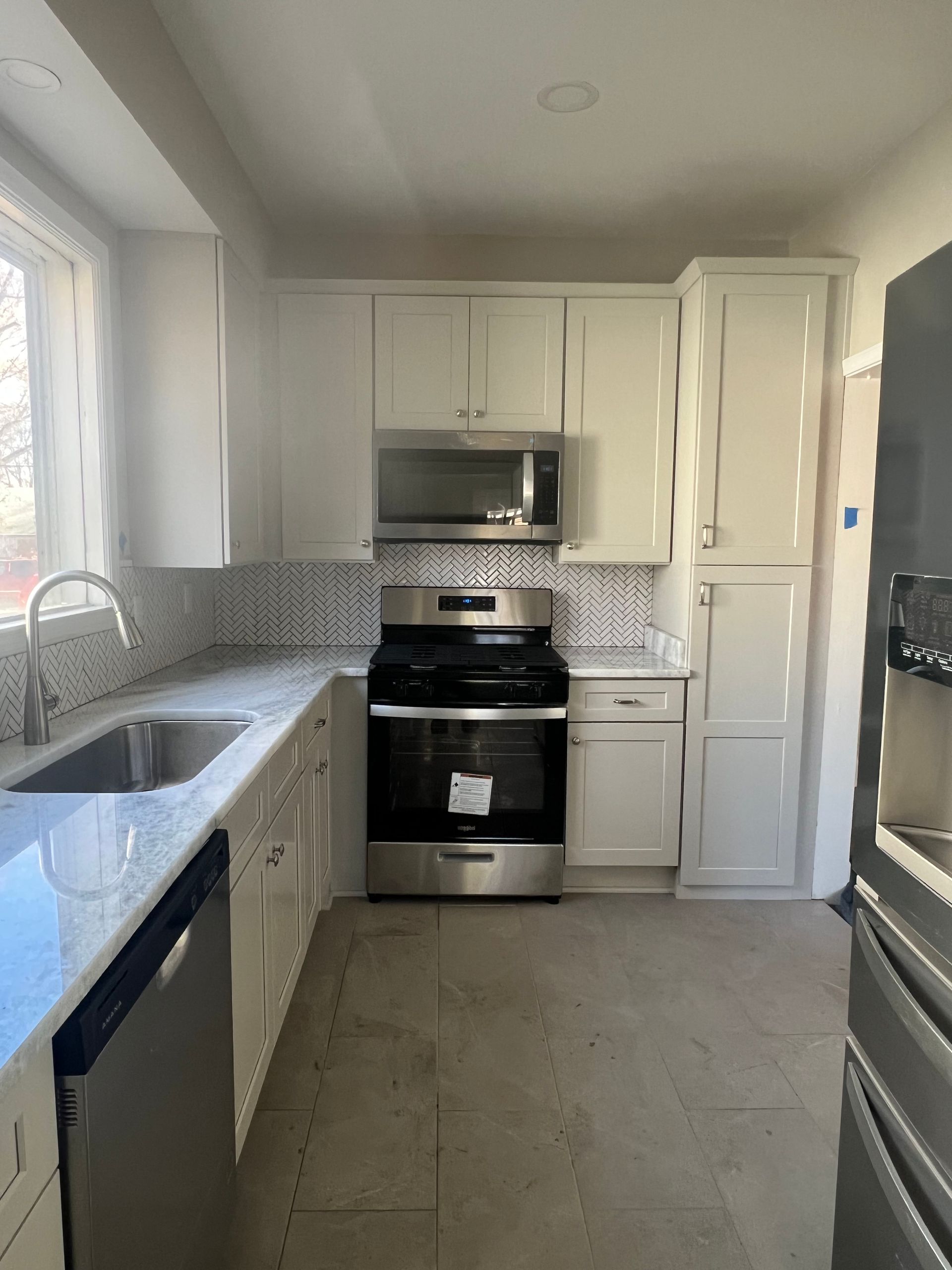 White kitchen with granite countertops, stainless steel appliances, and tile backsplash.