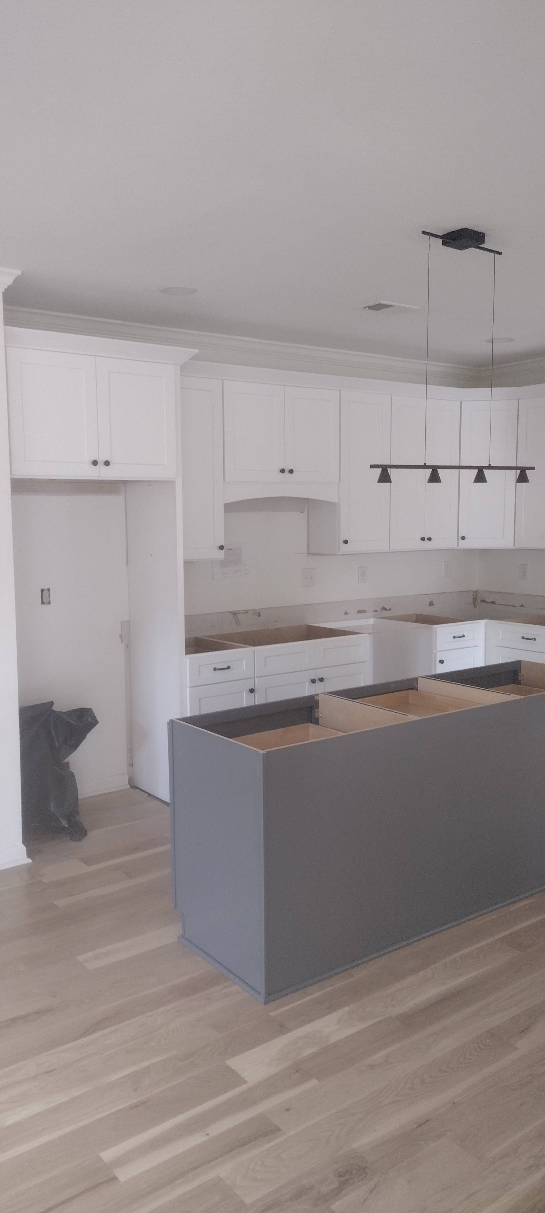 Kitchen remodel in progress, featuring white cabinets, gray island, and wood flooring.
