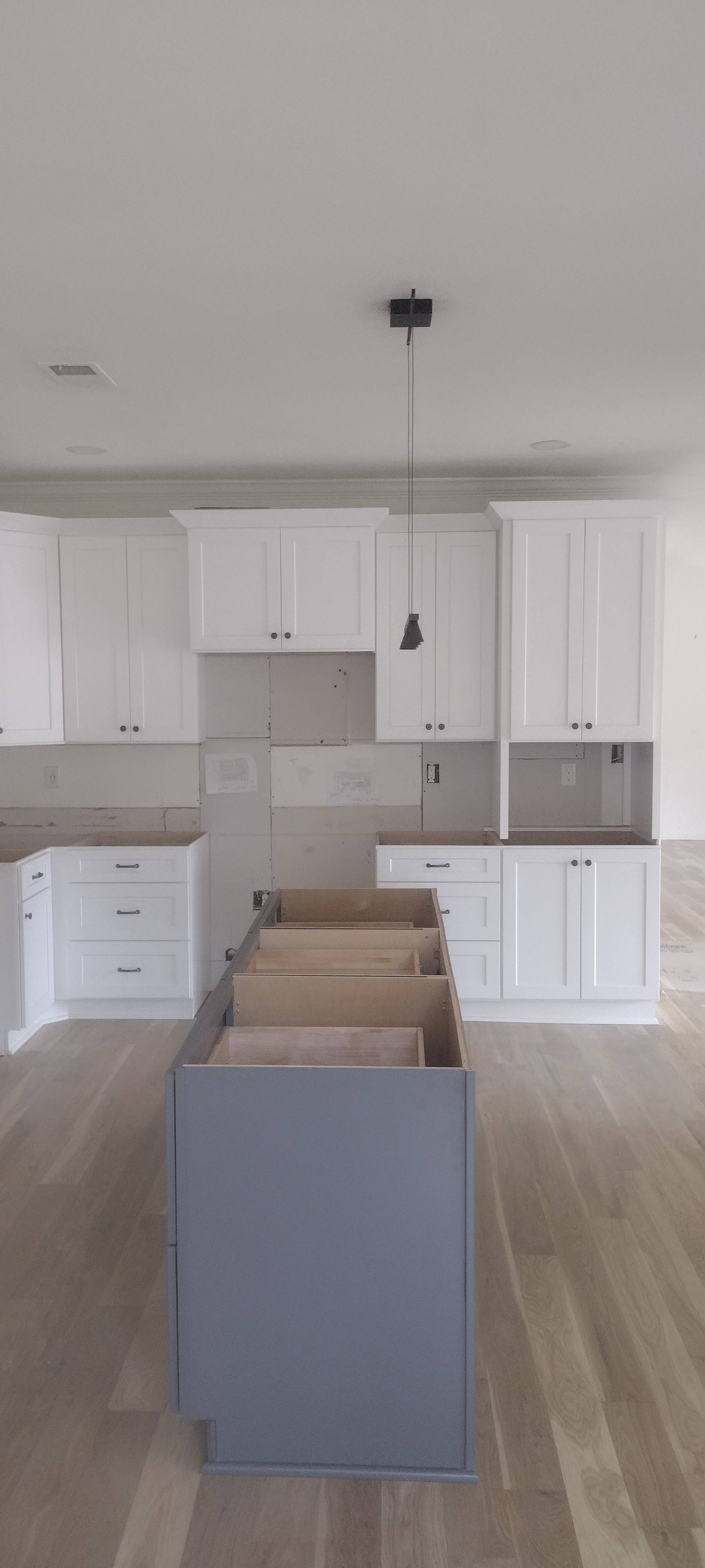 White kitchen cabinets with gray island and light wood floors.