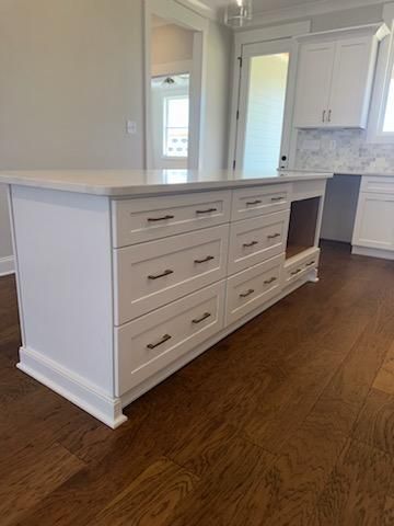 White kitchen island with drawers, dark hardware, and light countertop on wood floor.