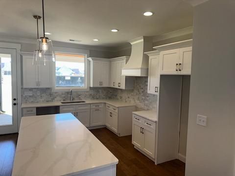 White kitchen with island, cabinets, marble backsplash, and stainless steel sink.