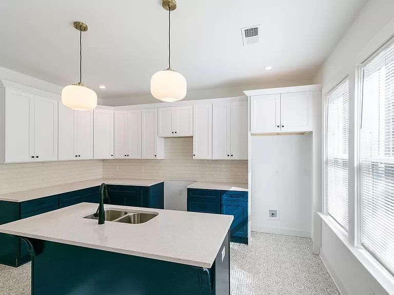 Modern kitchen with white and blue cabinets, island with sink, two pendant lights, and a window.