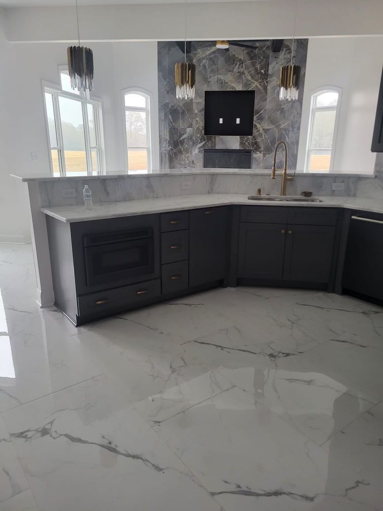 Dark gray kitchen cabinets with a marble countertop and flooring, microwave, and sink.