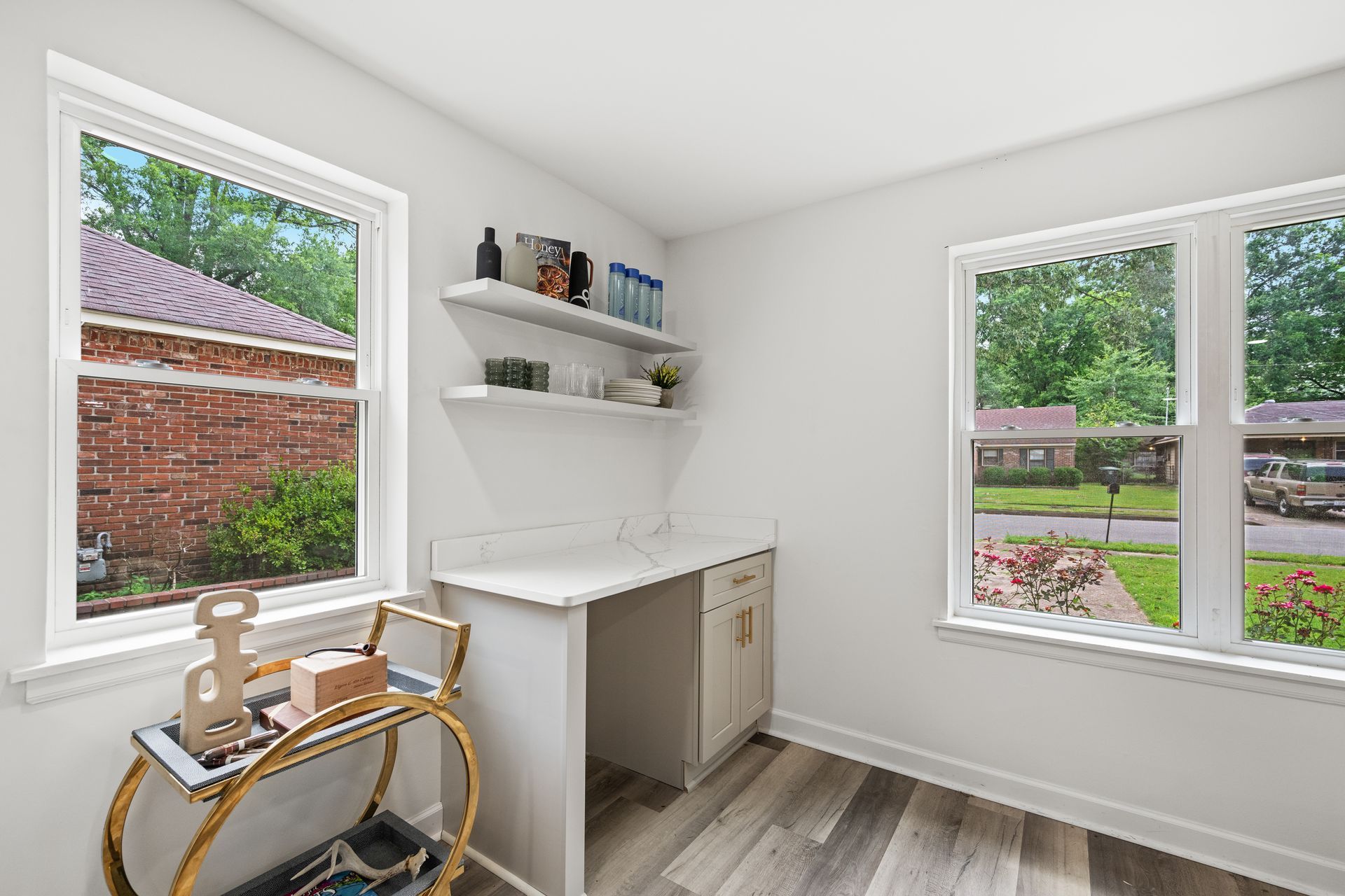 Bright white office with desk, floating shelves, and two windows.