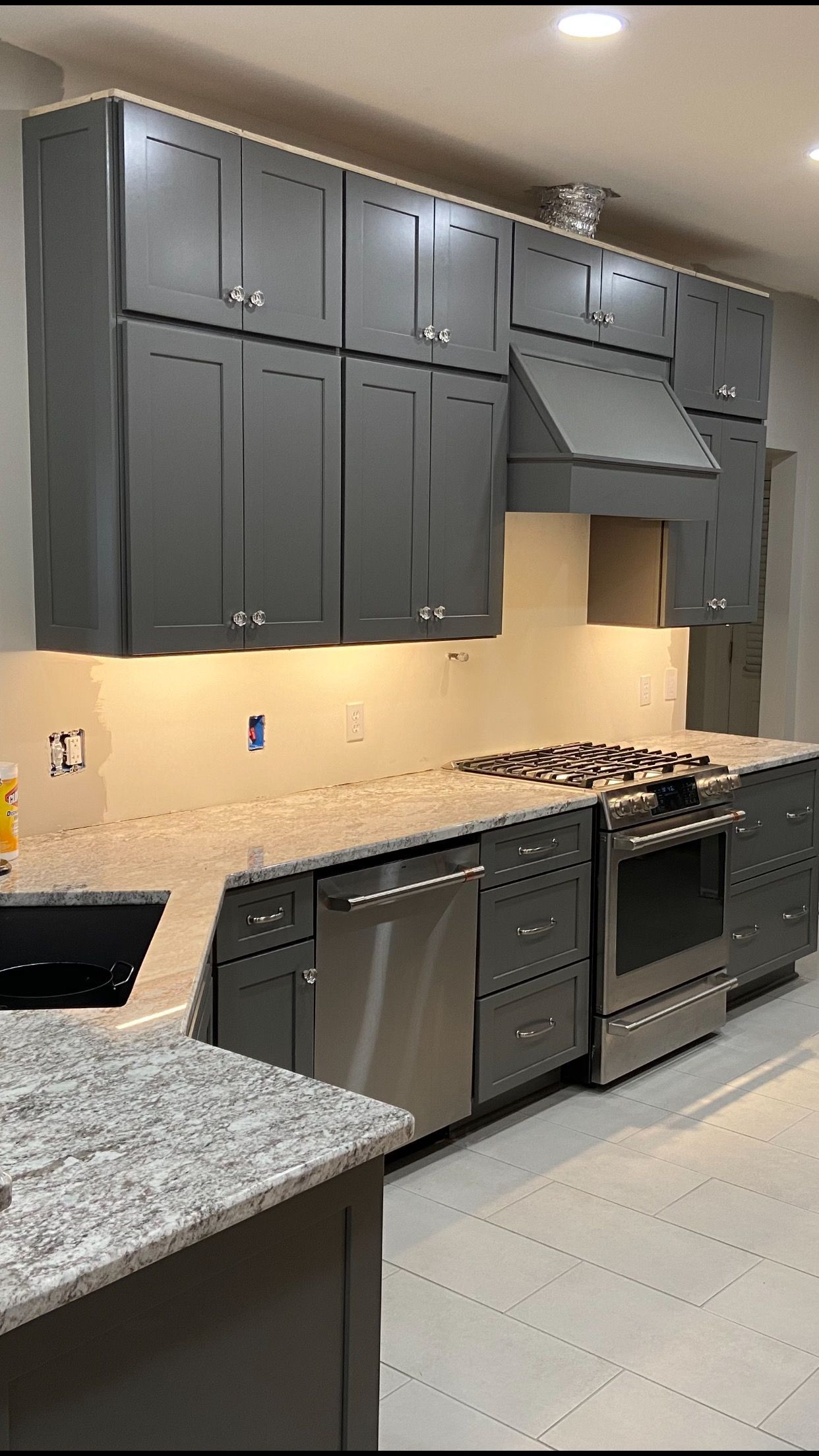 Gray kitchen cabinets and stainless steel appliances; a countertop and island with a granite finish.