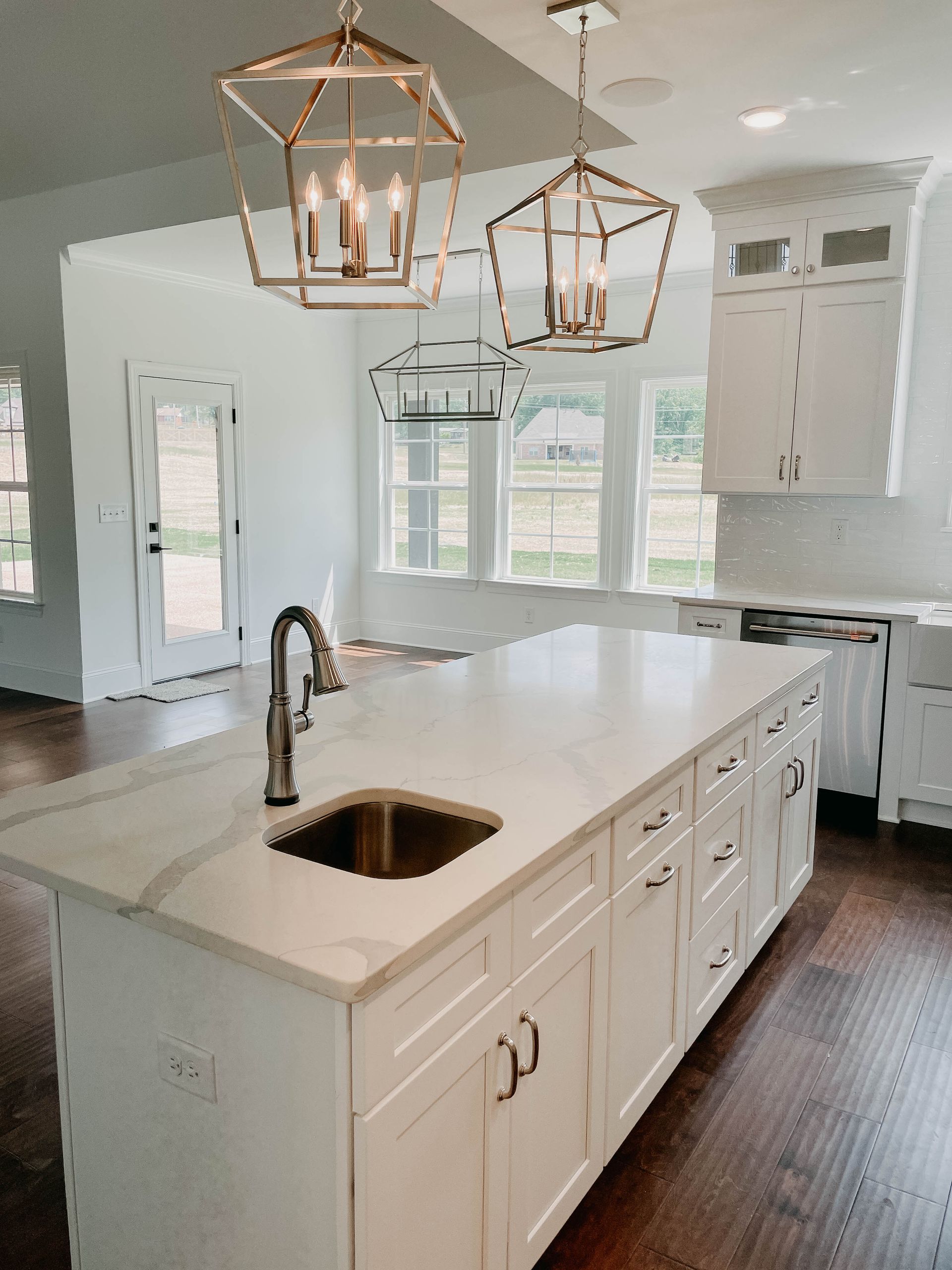 White kitchen island with a marble countertop, sink, and drawers. Overhead are two pendant lights.