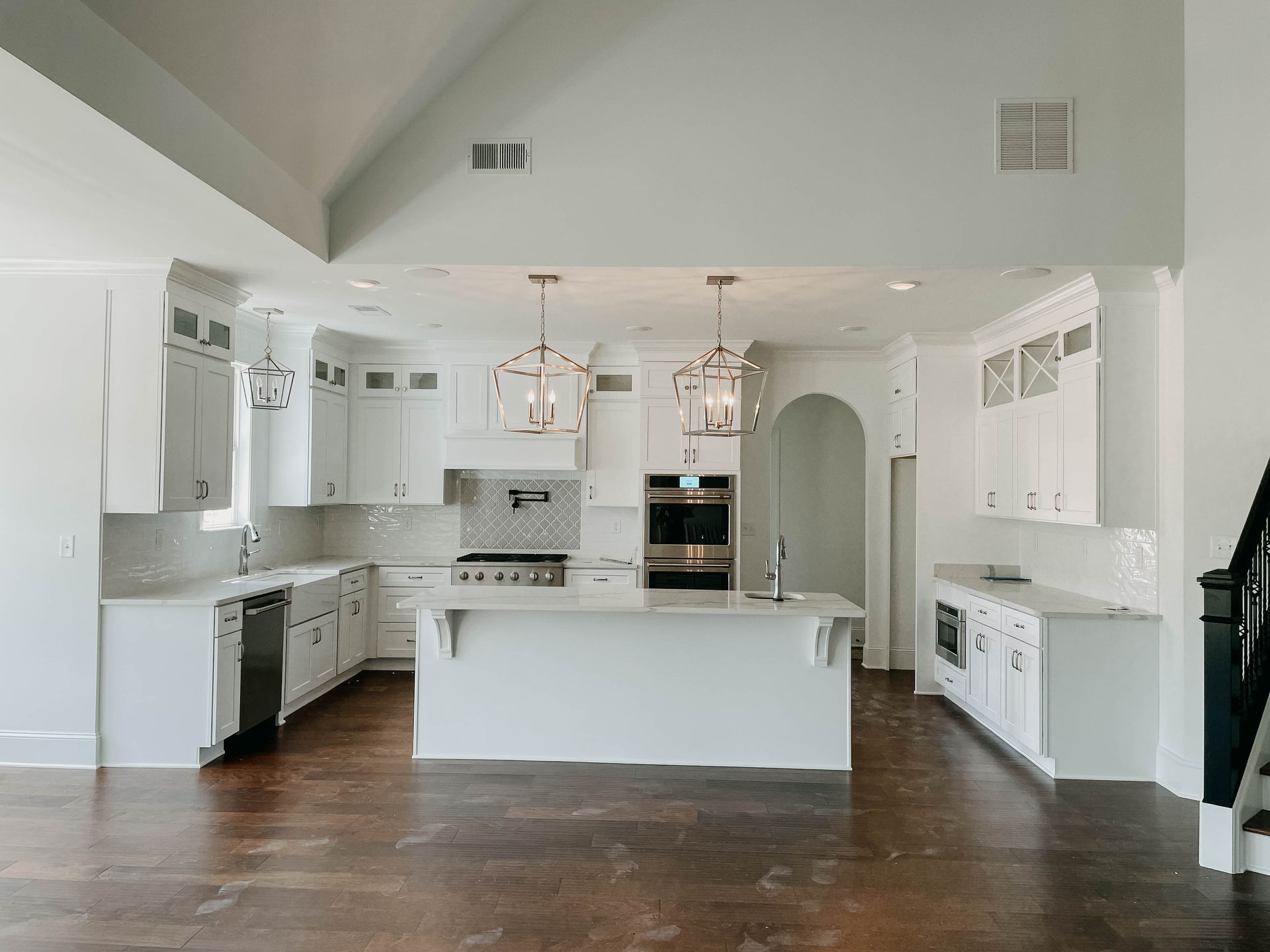 White kitchen with island, cabinets, and appliances on a dark wood floor. Two pendant lights hang over the island.