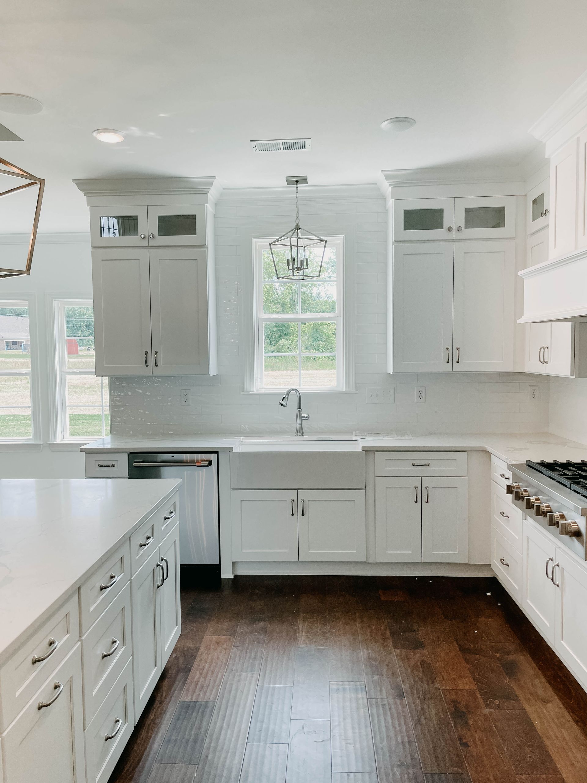 White kitchen with dark wood floors; stainless steel appliances, large sink, and a window.