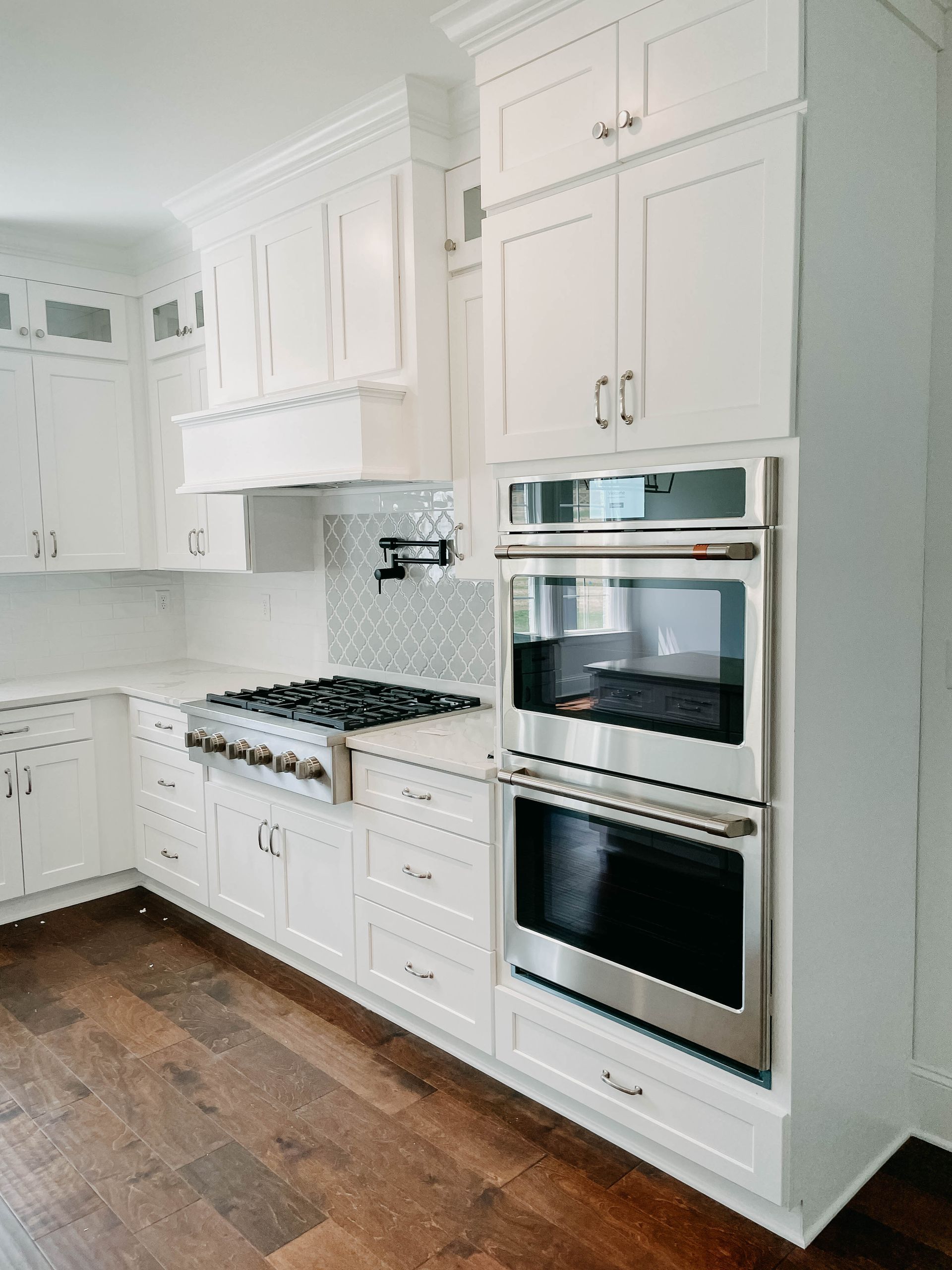 White kitchen with stainless steel double oven, stove, cabinets, and dark wood floor.