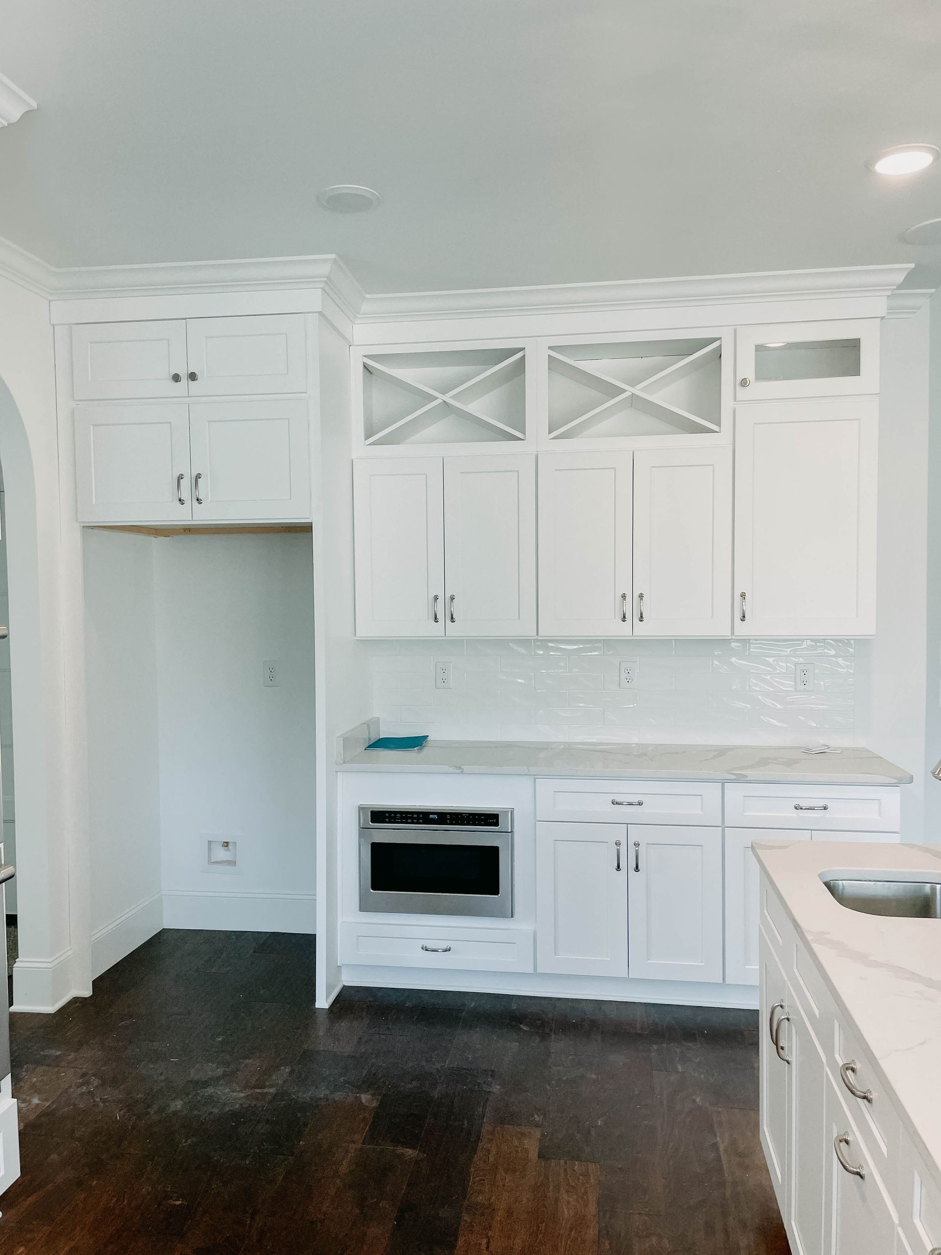White kitchen cabinets with microwave, wine rack, and countertop, built-in against a white wall.