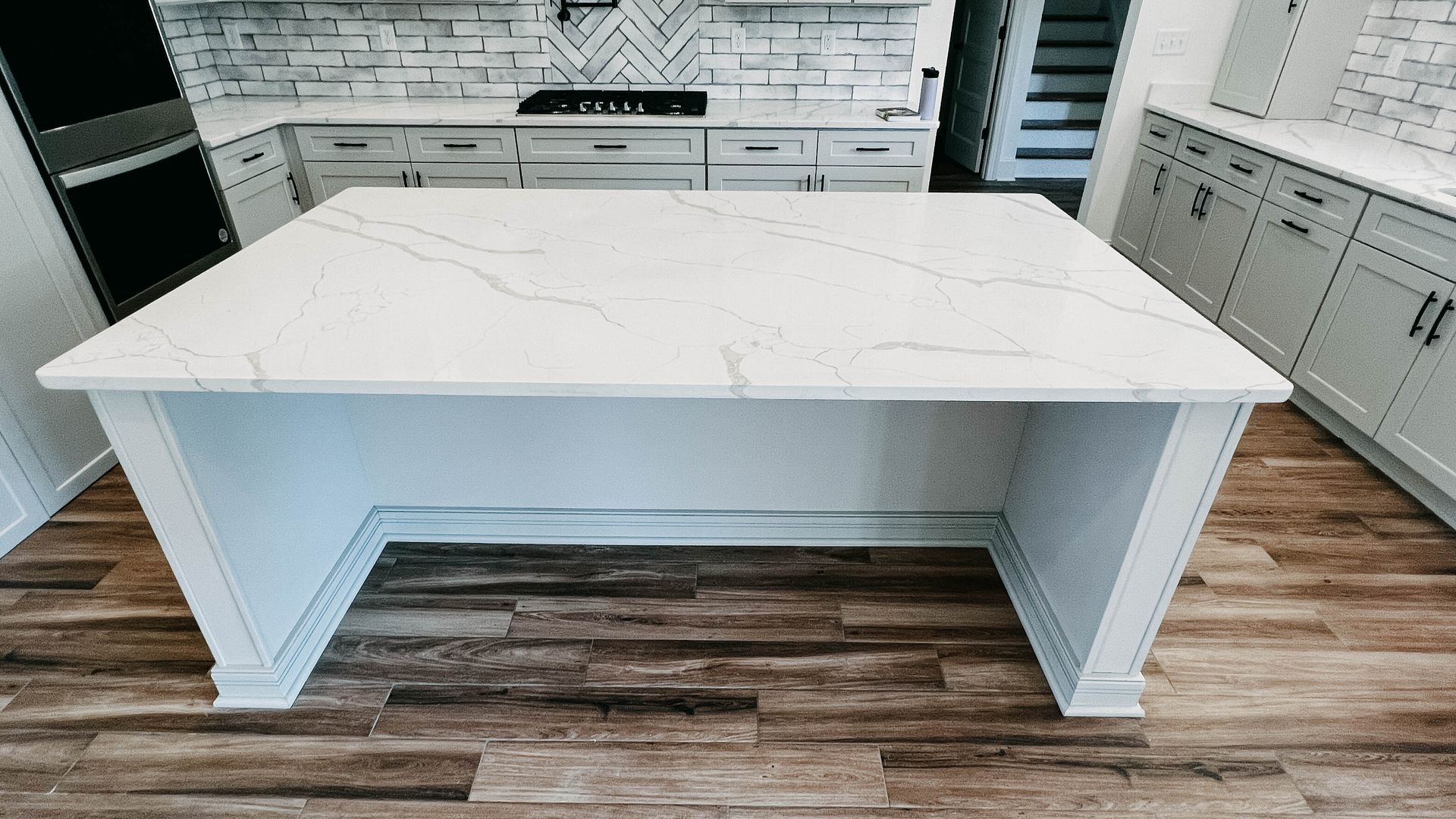 White kitchen island with marble countertop, wood floor, and light cabinets.