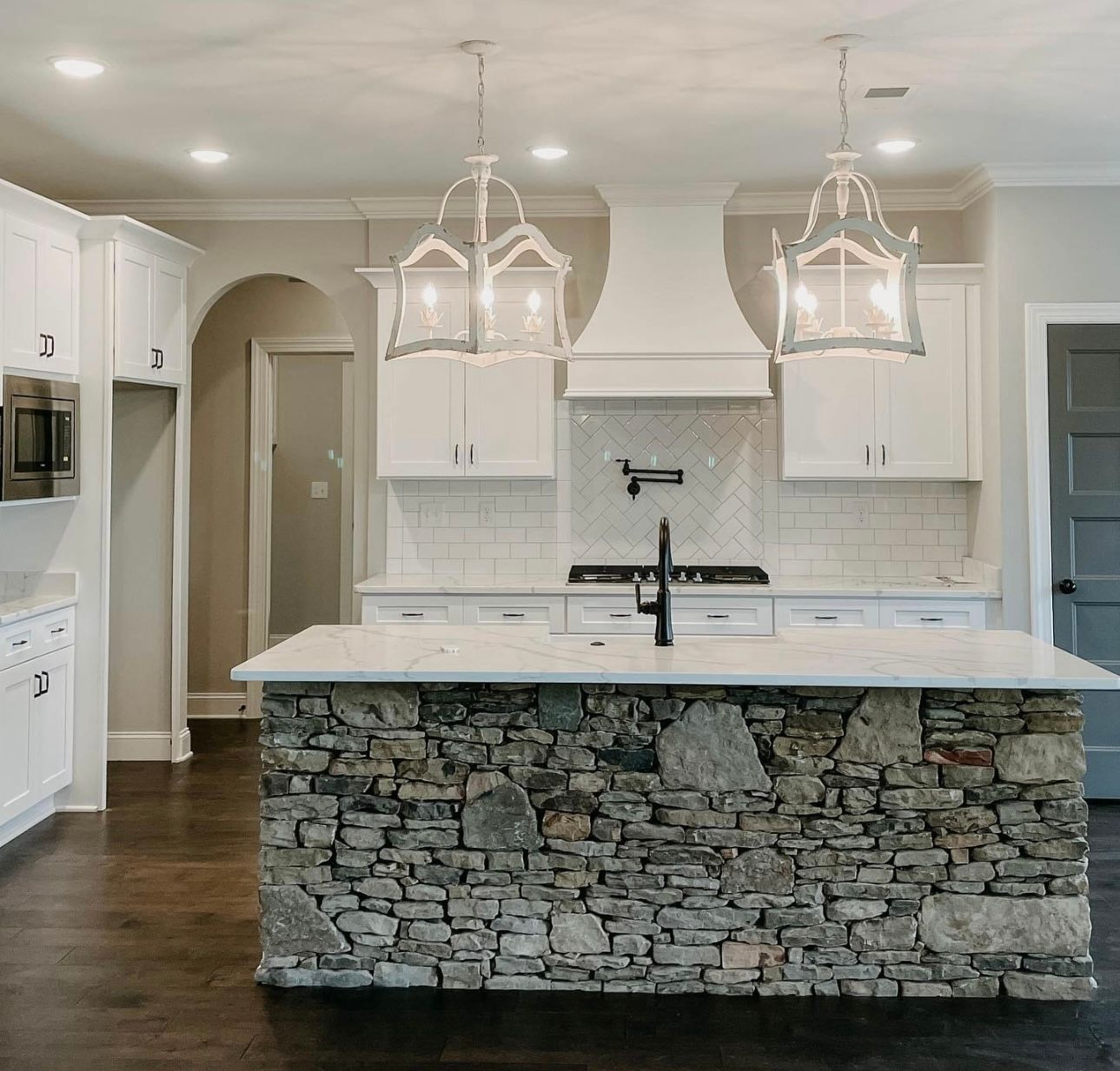 Kitchen with stone island, white cabinets, and two decorative hanging lights.