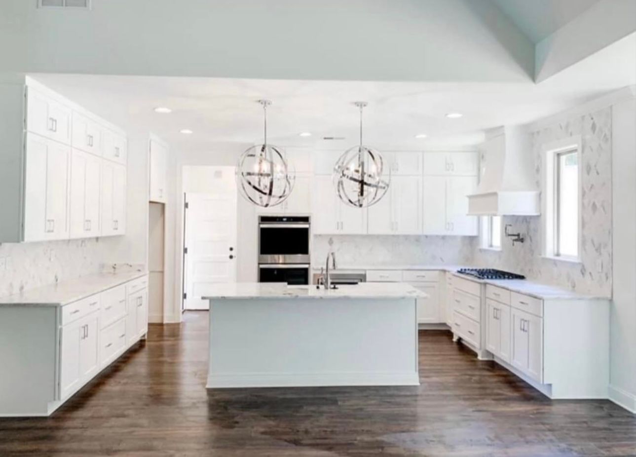 White modern kitchen with marble backsplash, cabinets, and island; wood floors.