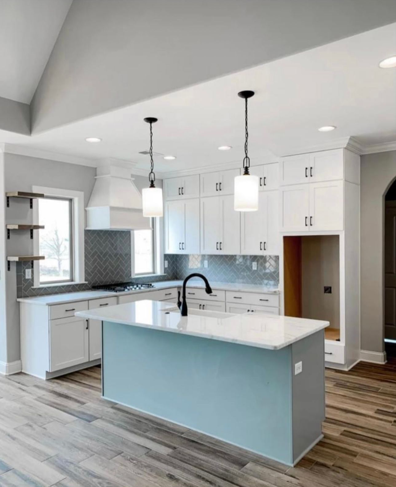 Modern kitchen with white cabinets, blue island, gray backsplash, and light wood flooring.