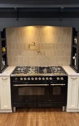 Black stove with gold accents, beige tile backsplash, cream cabinets, and wooden floors.