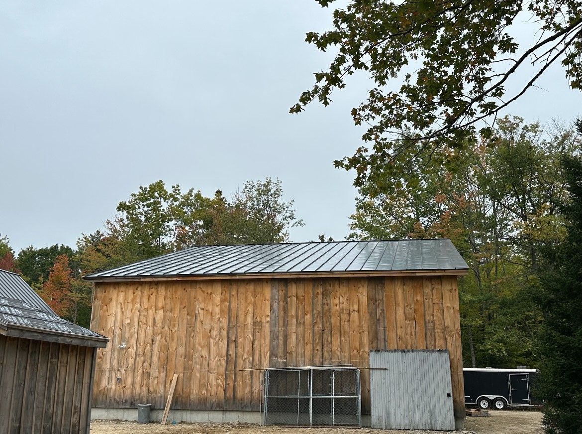 A wooden barn with a metal roof is surrounded by trees.
