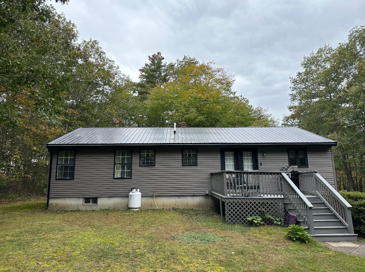 A small house with a metal roof is sitting in the middle of a grassy field.